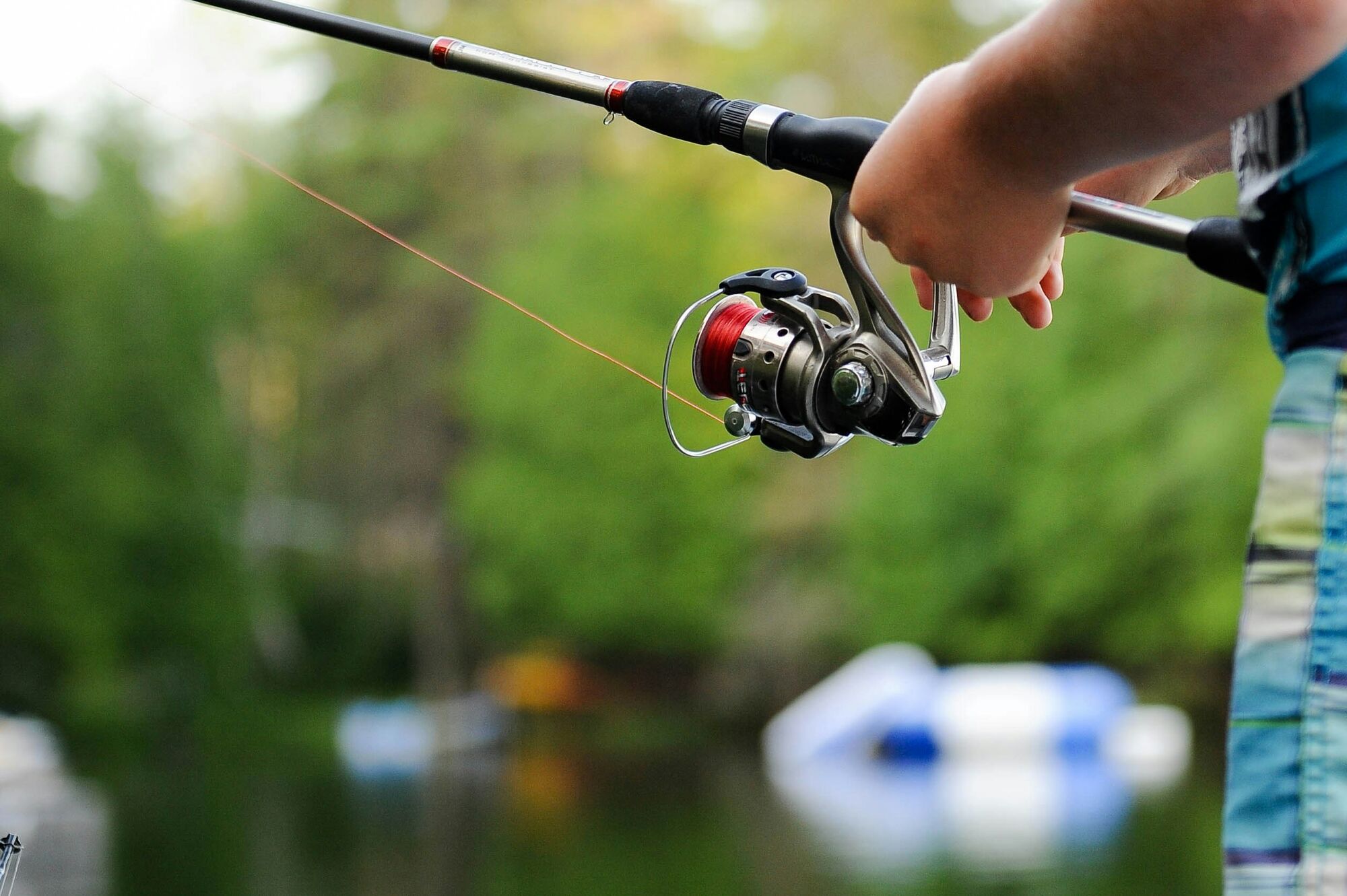 Hands on a spinning rod and reel, a lake blurred behind.